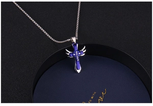 Dettaglio del ciondolo a croce blu e argento con ali e strass su una scatola