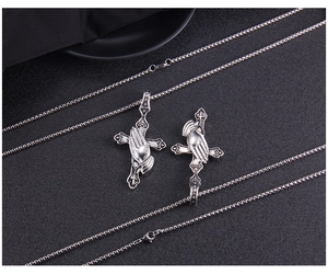 Detail of two punk style stainless steel box chains with praying hand cross pendants