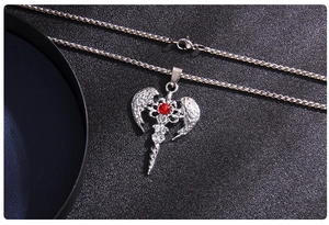 Close-up of angel wing cross pendant with red gemstone on black leather background