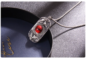 Macro detail of gothic stainless steel pendant featuring a red devil eye and eagle relief
