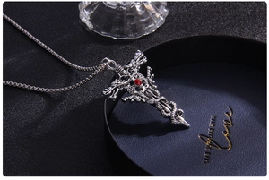 Close-up of gothic dragon cross pendant with central red crystal on a beaded chain
