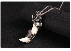 Close-up of retro silver dragon pendant with white wolf tooth on a black texture