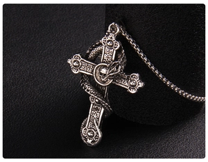 Macro detail of gothic silver cross pendant with coiled snake and skull on box chain
