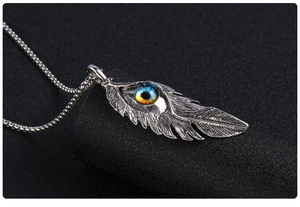 Détail macro du collier pendentif plume vintage avec œil maléfique sur fond noir