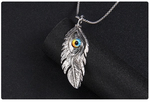 Gros plan de pendentif plume vintage en acier avec œil maléfique sur fond noir