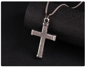 Macro detail of silver cross pendant with grid texture on black leather background