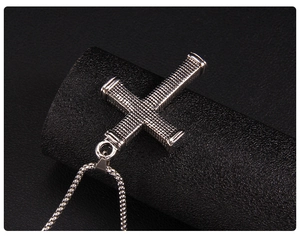 Detailed close-up of a silver cross pendant with grid texture on a black box chain