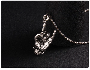 Close-up of rock punk style stainless steel skull hand gesture pendant on box chain