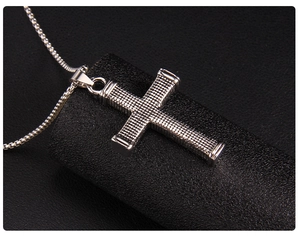 Macro detail of silver steel cross pendant with textured checkered pattern and box chain
