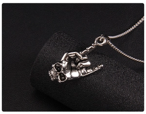 Macro detail of punk rock stainless steel necklace featuring a skull hand gesture pendant