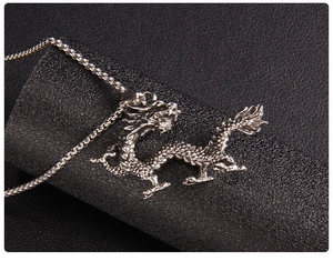Macro shot of silver dragon pendant necklace on black textured surface showing fine details