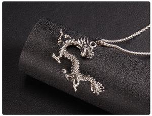 Detailed macro view of an intricate silver dragon pendant on a black leather surface