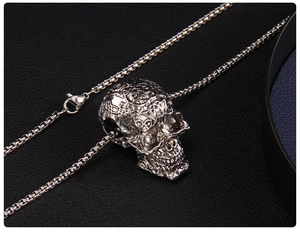 Detailed close-up of a silver skull pendant with intricate relief and black box chain