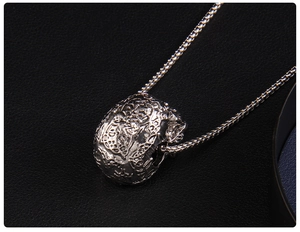 Close-up of a silver skull pendant with intricate hollow carvings and a metal chain