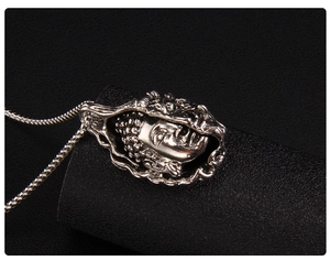 Macro shot of silver Buddha pendant necklace with hollow wavy frame on black texture