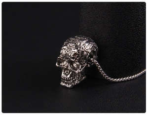 Close-up of a silver gothic skull pendant with vintage engraved patterns and a box chain