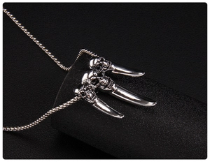 Macro shot of three detailed punk skull heads with sharp claws on polished steel necklace