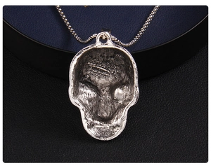 Detailed macro of vintage silver skull pendant with box chain on a blue velvet jewelry box