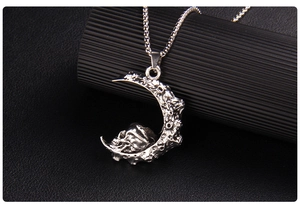 Macro shot of gothic silver crescent moon pendant with a detailed skull on black texture