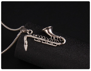 Macro detail of silver saxophone pendant necklace showing vintage texture and snake chain