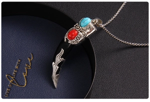Detail of vintage wolf tooth pendant with silver floral relief and colorful stones