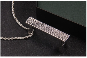 Macro detail of silver bench pendant with wood grain texture on rope chain necklace