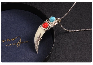 Close-up of wolf tooth pendant with blue turquoise, red gem and vintage silver details