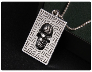 Macro view of a rectangular silver skull pendant with intricate braided edge texture