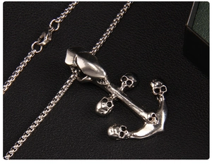 Macro shot of silver anchor skull pendant on box chain over black leather background