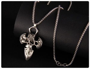 Detailed macro of silver skull cross pendant with box chain on black leather background