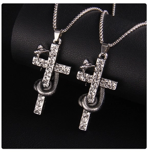 Macro shot of silver punk cross pendant wrapped with snake on black leather background