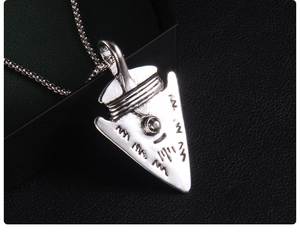 Macro detail of vintage silver arrow pendant necklace with tribal carving on black background