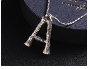Vista macro del ciondolo lettera A argento con trama di bambù su astuccio