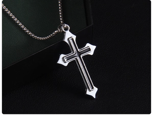 Gros plan d'un pendentif croix argentée avec insert noir sur une chaîne à billes en métal