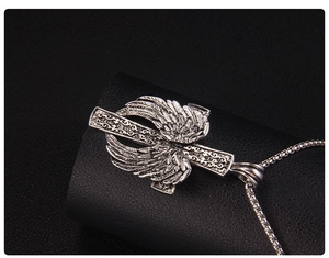 Vue macro d'un pendentif croix gothique avec ailes de plumes sur une chaîne de type box