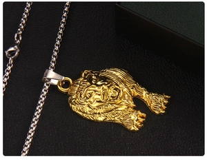 Détail macro d'un pendentif tête de lion plaqué or avec une chaîne box en acier argenté