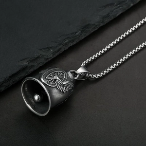 Vintage stainless steel guardian bell necklace with winged wheel relief on stone surface