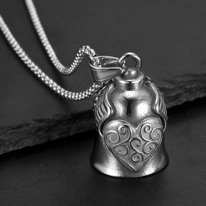 Macro detail of retro stainless steel heart bell pendant with wing design on dark rock