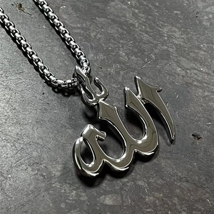 Macro view of silver Allah pendant on box chain over grey textured stone background