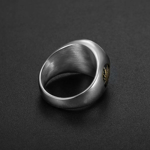Vue macro d'une bague en acier brossé avec motif de feuille dorée sur fond noir