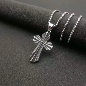 Vue macro du pendentif croix en argent avec stries radiales et texture perlée sur chaîne ronde