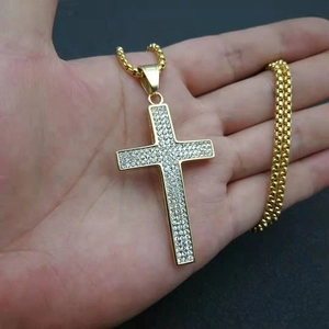Détail d'un pendentif croix hip-hop plaqué or serti de zircons tenu à la main