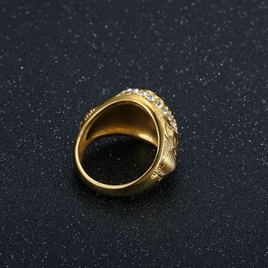 Dettaglio dell'anello dorato a forma di aquila con strass bianchi su sfondo nero