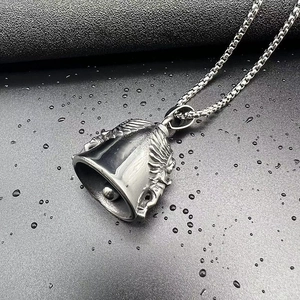 Vue macro du pendentif cloche ange en acier argenté sur fond noir avec gouttes d'eau