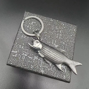 Fish-shaped stainless steel bottle opener keychain on black gift box, 45-degree angle