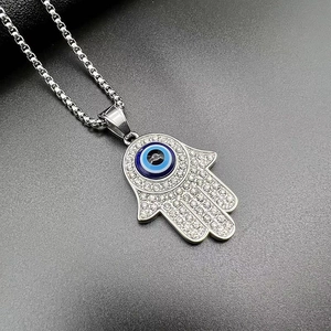 Macro detail of silver Hamsa Hand pendant with rhinestones and blue Evil Eye on box chain