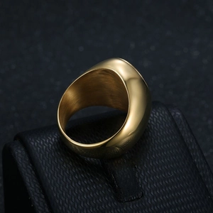 Polished gold plated stainless steel signet ring for men on a dark geometric jewelry stand