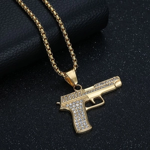 Nahaufnahme der goldenen Box-Halskette mit 1911 Pistolen-Anhänger und weißen Kristallen
