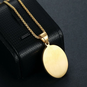 Macro detail of a gold-plated oval pendant featuring a brushed metal finish on a box chain