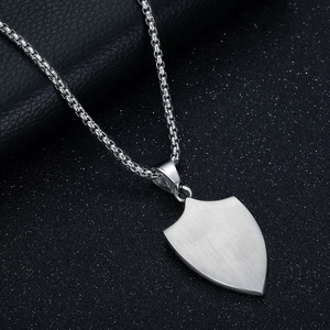 Macro shot of brushed shield pendant with silver box chain on black textured background